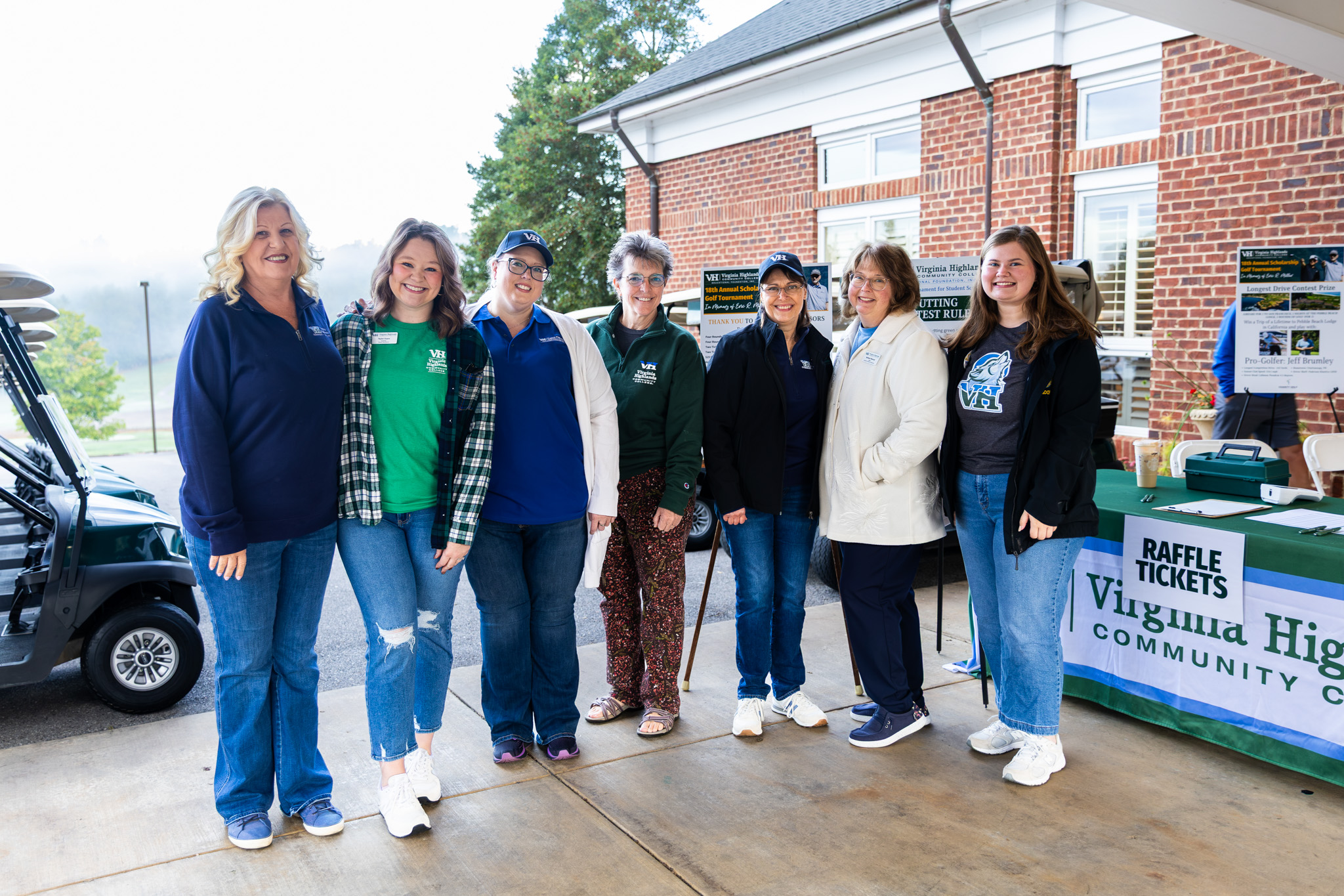 A group of seven women posing together for a portrait outdoors under a covered pavilion next to a Virginia Highlands Community College check-in table and golf carts.