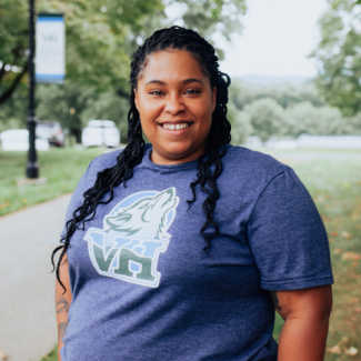 Alesha Russell, a woman with long dark braids, wearing a blue t-shirt with a VHCC wolf logo.