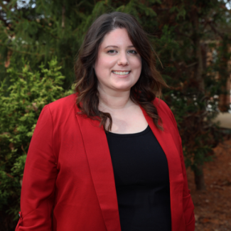 Courtney Ricks, a woman with wavy dark hair, wearing a red blazer over a black top.