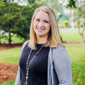 Danielle Pennington, a woman with blonde hair, wearing a black shirt and a grey cardigan with a long beaded necklace.