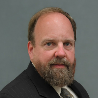 Headshot of James Baker, a man with a grey beard and balding grey hair, looking directly at the camera with a neutral expression. He is wearing a dark pinstripe suit jacket, a white collared shirt, and a grey patterned tie, set against a solid grey studio background.