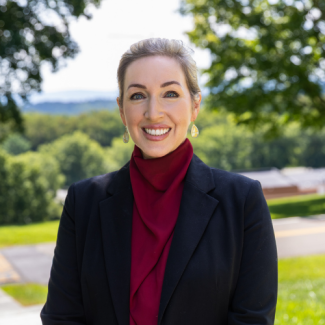 Headshot of Nicole Watson, a smiling woman with hair in an updo wearing teardrop earrings, a black blazer, and a red high-neck top.