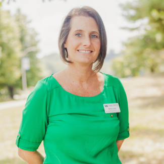 Tamara Lasley, a woman with short brown hair, wearing a green blouse and a name tag, smiling in an outdoor park-like setting.