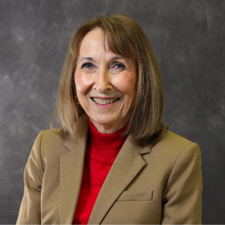 Winona Fleenor, a woman with shoulder-length brown hair, wearing a red turtleneck and a tan blazer, smiling against a dark grey textured background.